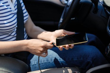 Bir kadın akıllı telefonunu arabada şarj ediyor, USB kablosuna bağlanıp yolculuk sırasında cihazını çalıştırıyor. Yolda modern kolaylık