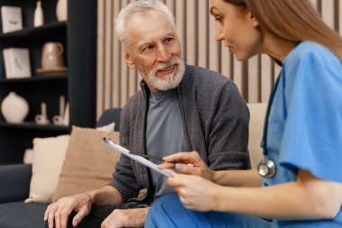 Ev ziyareti sırasında gülümseyen yaşlı bir adama yardım eden genç hemşire, yaşlı hastalara sağlık ve destek sağlıyor. Sağlık hizmeti kavramı