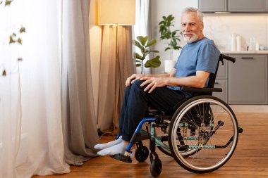 Tekerlekli sandalyede oturan sakallı yaşlı bir adam, modern bir dairede dinlenirken huzur saçıyor, ev ortamının rahatlığını ve sıcaklığını kucaklıyor. Destek konsepti