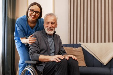 Genç, gülümseyen bir hemşire tekerlekli sandalyedeki mutlu yaşlı bir adamın yanında duruyor. İkisi de rahat bir oturma odasında kameraya bakıyor. Evde bakım hizmetini somutlaştırıyor. Yardım kavramı