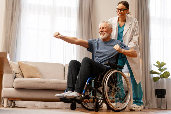 Happy senior man sitting in a wheelchair, exercising with the assistance of a caring female nurse in a bright and inviting living room, fostering wellbeing and independence