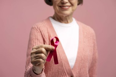 Göğüs kanseri farkındalığı kampanyasını desteklemek için pembe kurdele gösteren gülümseyen son sınıf öğrencisi kadın. Tedavi kavramı