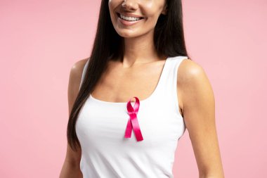 Gülümseyen bir kadının beyaz atletinin üzerinde pembe bir kurdele sergilemesi, göğüs kanseri farkındalığını ve hastalıktan etkilenenlere verdiği desteği temsil ediyor.
