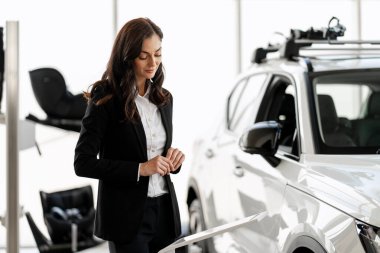 Modern bir galeride potansiyel müşterilere yeni bir araba sunarken kollarını düzelten profesyonel bir satış elemanı.