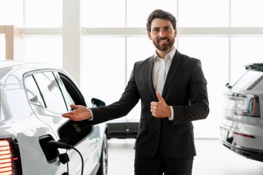 Otomobil satıcısı elektrik yüklü araba gösteriyor ve bayilikte onay veriyor, sürdürülebilir ulaşım ve çevre dostu araçları destekliyor