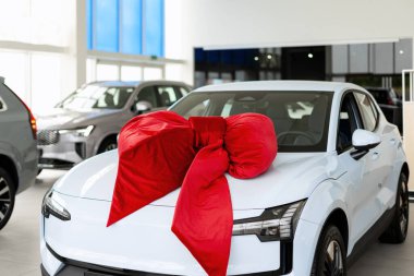 Kaputta büyük kırmızı bir fiyonk ile süslenmiş beyaz elektrikli araba. Geniş, modern bir araba galerisinin içine park edilmiş.