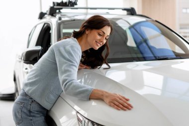 Yeni arabasının kaputunu okşayan mutlu müşteri, lüks bir galeride aldığı zevkin tadını çıkarıyor.