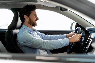 Parlak, güneşli bir günde gösterişli, modern bir araba süren işadamı, direksiyonu sıkıca kavrıyor ve zevkle gülümsüyor.