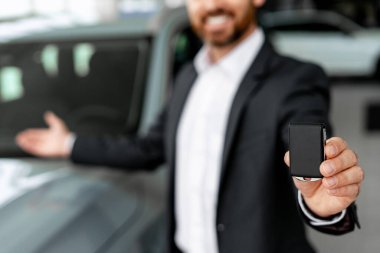 Araba satıcısı galeride ilgilenen bir müşteriye yeni bir aracı hevesle gösterirken araba anahtarlarını sunuyor.