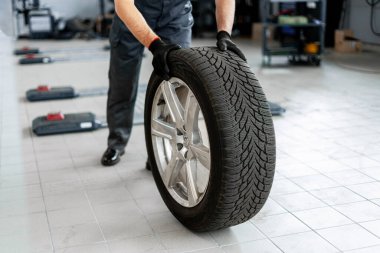 Profesyonel tamirci bir araba servisinde özenle çalışıyor, kış lastiklerini değiştiriyor ve optimal araç performansı ve güvenliğini sağlıyor
