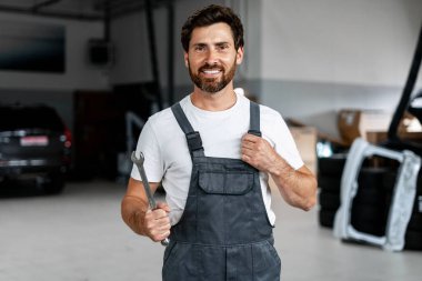 Araba tamirhanesinde anahtar tutan gülümseyen bir tamircinin portresi, otomotiv bakımında uzmanlık ve profesyonellik sergiliyor.