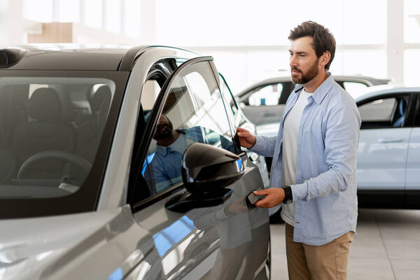 Male customer inspecting a new car inside an auto showroom, engaging in the process of purchasing a modern vehicle for transportation