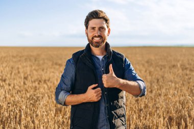 Güneşli bir günde altın buğday tarlasında dikilirken gülümseyen bir çiftçinin portresi başarılı bir hasatta memnuniyet ve gurur yayar.