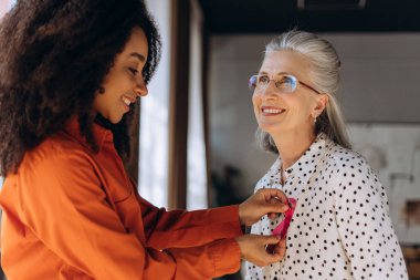 Genç Afrikalı Amerikalı gönüllü, gülümseyen yaşlı kadının tişörtüne pembe kurdele takarak meme kanseri araştırmaları ve destekleri için farkındalık yaratıyor. Destek konsepti