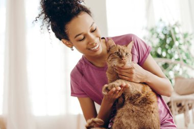 Mutlu Afro-Amerikalı genç bir kadının portresi. Evde yoga minderinde sevimli kızıl kedisiyle sessiz vakit geçiriyor. Spor, sağlıklı bir kavram.