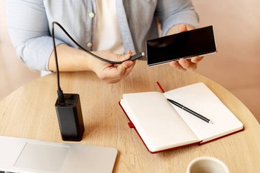 İşadamı bilgisayarla ve defterle çalışırken akıllı telefonu elektrik bankasıyla şarj ediyor.