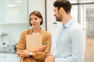 İş kadını elinde bir pano tutuyor ve iş adamıyla konuşuyor, modern ofiste projeyi tartışıyor, ortak görev üzerinde işbirliği yapıyor, iş büyümesi için fikir ve stratejileri paylaşıyor. Beyin fırtınası konsepti