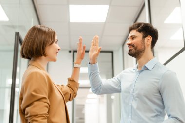 İki neşeli iş adamı, modern ofis koridorunda başarılı bir başarıyı kutlayarak, takım çalışmasını ve motivasyonunu ifade ederek beşlik çakıyor.