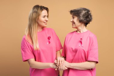 Pembe kurdelelerle süslenmiş pembe tişörtler giyen iki gülümseyen kadın, göğüs kanseri farkındalığı ve umut için verilen mücadelede el ele tutuşuyor, destek ve birlik oluyor. Sağlık hizmeti kavramı