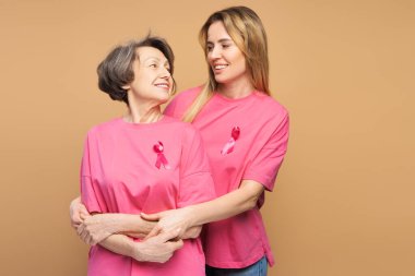 Kızı, pembe kurdeleli pembe tişörtler giyerken yaşlı annesine sarılıyor ve meme kanseri farkındalığı ve araştırmalarına destek veriyor. Sağlık hizmeti kavramı