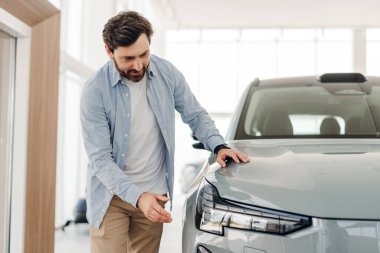 Potansiyel alıcı araba galerisinde yeni bir elektrikli aracı kontrol ediyor, kaputa dokunuyor ve satın alma kararı vermeden önce ön ışıkları kontrol ediyor. Alışveriş konsepti