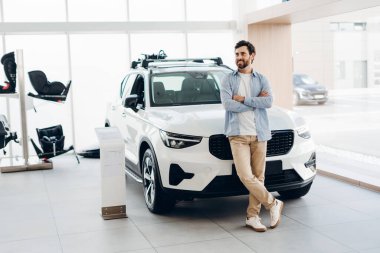 Araba galerisinde çatı rafı olan beyaz bir SUV 'a yaslanan mutlu müşteri arka planda bebek oto koltukları sergileniyor. Konsept satın alınıyor