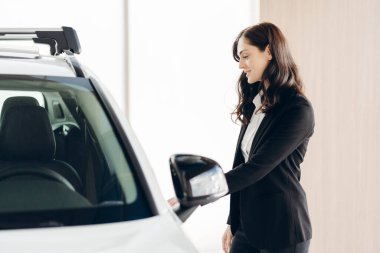 Modern araba galerisindeki potansiyel müşterilere yeni beyaz araba özelliklerini sunan profesyonel satış elemanı, araç faydalarını ön plana çıkarıyor ve kapanış anlaşmasını yapıyor. Ulaşım kavramı