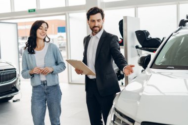 Kadın müşteriye yeni bir araba gösteren profesyonel bir satıcı, modern bir bayide özellikleri ve seçenekleri tartışıyor, pozitif bir satış deneyimi yaratıyor. Ulaşım kavramı