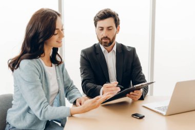 Finansal danışman, parlak bir ofiste yapılan bir toplantıda müşteriye sözleşme detaylarını açıklıyor, yatırım fırsatları ve mali planlamayı tartışıyor. Anlaşma konsepti
