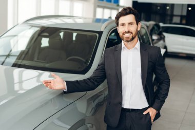 Gülümseyen profesyonel araba satıcısı galerideki potansiyel müşterilere yeni bir araba gösteriyor, otomotiv perakende işini teşvik ediyor ve mükemmel müşteri hizmetleri sunuyor. İş konsepti
