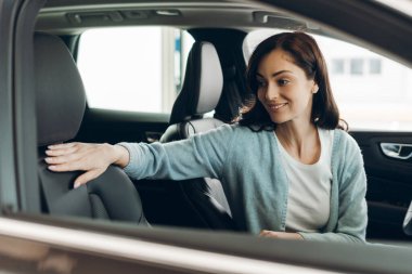 Gülümseyen kadın araba satın alma işlemi sırasında lüks ve kaliteli bir deneyim yaşarken araba koltuğunun rahatlığını kontrol ediyor. Ulaşım kavramı