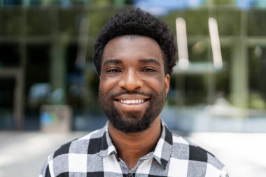 Kendine güvenen genç Afrikalı Amerikalı işadamı modern bir ofis binasının önünde dururken gülümsüyor, profesyonellik ve başarı yayıyor.