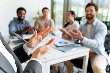 Modern ofiste başarılı bir sunum yaptıktan sonra çok ırklı meslektaşlarından alkış alırken el kol hareketi yapan iş kadını