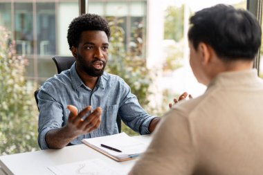 Modern bir ofisteki masada doküman ve grafikleri kullanarak birlikte çalışmayı tartışan iki iş adamı.