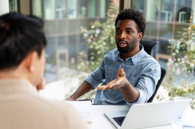 İş adamı, modern bir ofiste bilgisayar ve belge kullanarak iş arkadaşına stratejiyi açıklıyor.