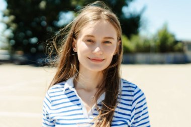 Hafif bir esinti, çizgili gömlek giyen, güneşli bir günün tadını çıkaran, uzun kahverengi saçlı, gülümseyen bir bayanın sakin ve kaygısız atmosferini yaratıyor. Doğal güzellik konsepti