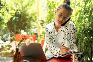 Bir kafede uzaktan çalışan, iş yöneten ve telefon görüşmeleri sırasında not alan serbest çalışan biri. Çevrimiçi teknoloji kavramı