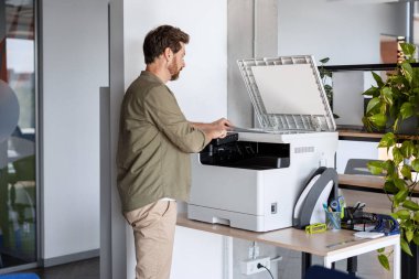 Modern ofis ortamında fabrikalarla çevrili çok fonksiyonlu bir yazıcıyı tamir eden bir ofis çalışanı pürüzsüz bir işlevsellik ve verimlilik sağlıyor.