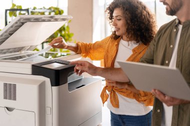 İki iş arkadaşı, profesyonel bir ortamda takım çalışması ve verimliliği vurgulayan çok fonksiyonlu modern bir yazıcı kullanıyorlar.