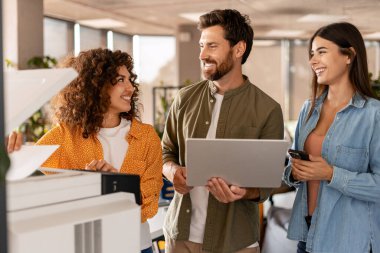 Fotokopi makinesi ve dizüstü bilgisayar kullanan mutlu iş adamları, fikirleri paylaşıyor ve ofiste bir projeyi tartışıyorlar.