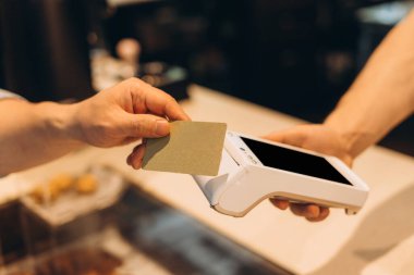 Müşteri, pastanedeki bir postane terminalinde kredi kartıyla temassız ödeme yapıyor. Lezzetli ikramlar sunarken hızlı ve güvenli bir alışverişin tadını çıkarıyor.