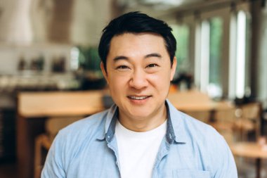 Modern bir ofis alanında gülümseyen kendine güvenen Asyalı işadamı, profesyonelliği ve başarıyı yayarken kurumsal bir ortamda pozitif ve neşeli bir atmosferi somutlaştırıyor.