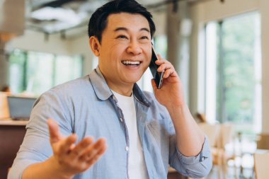 Asyalı serbest çalışan, elini bir arada tutarak gülümsüyor ve telefonda konuşuyor. Verimli bir sohbetin tadını çıkarıyor.