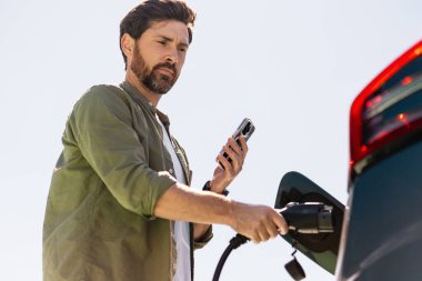 Kabloyu elektrikli araca bağlayan sürücü ve elektrik şarj noktasında cep telefonu uygulaması