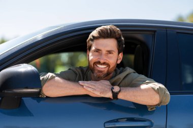 Gülümseyen bir adam arabasının camından sarkıyor, yaz yolculuğunun keyfini çıkarıyor, mutluluk saçıyor ve tasasız bir macera yaşıyor.