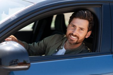 Yakışıklı iş adamı, modern elektrikli bir aracın içinde araba sürüyor ve gülümsüyor güneşli günün tadını çıkarıyor ve açık yolların özgürlüğünü kucaklıyor.