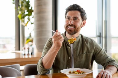 Neşeli sakallı adam modern bir restoranda lezzetli ve sağlıklı bir makarna yemeğinin tadını çıkarıyor. Sağlıklı ve hayat tarzını somutlaştırıyor.