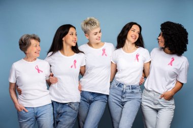 Beyaz tişörtlerine pembe kurdele takmış beş gülümseyen kadın birbirlerine sarılıyor ve göğüs kanseri farkındalığını destekliyorlar.