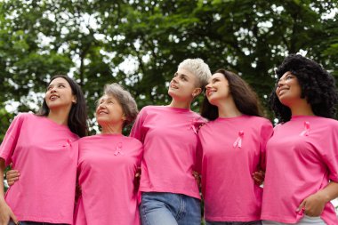 Bir grup gülümseyen gönüllü pembe kurdeleler takıp parka bakıyorlar. Destek konsepti