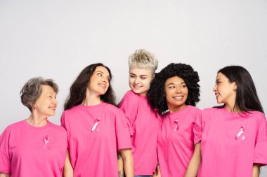 Bir grup mutlu çokuluslu kadın pembe göğüs kanseri farkındalığı takıyor. Destek konsepti